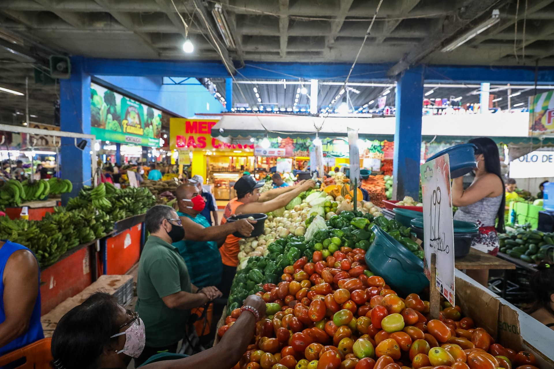 Foto tirada no mercado municipal de Jaboatão dos Guararapes, em Pernambuco, mostra consumidores selecionando cebolas, pimentões, tomates e outros vegetais, enquanto uma feirante observa a cena