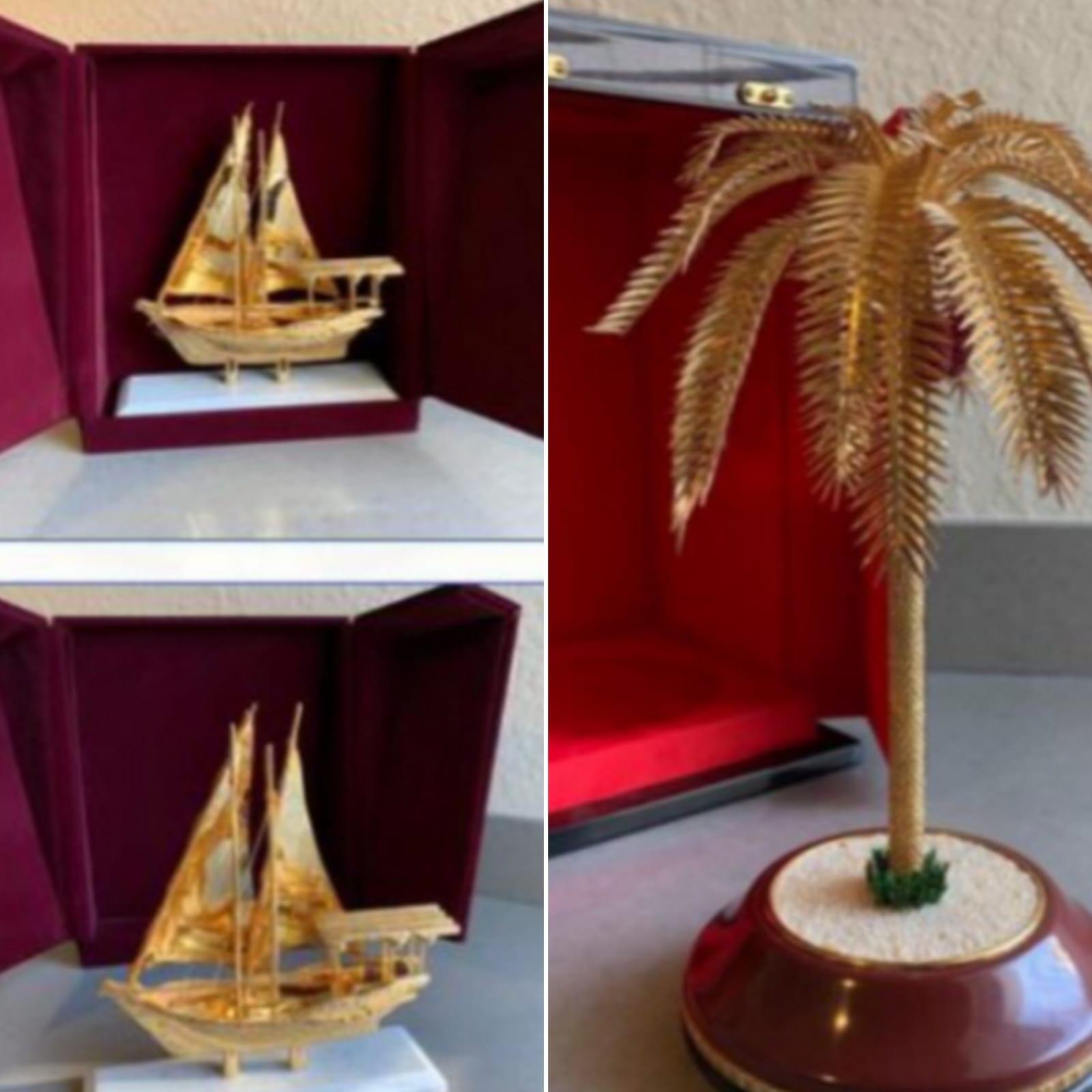 Imagem mostra esculturas douradas de um barco e uma palmeira
