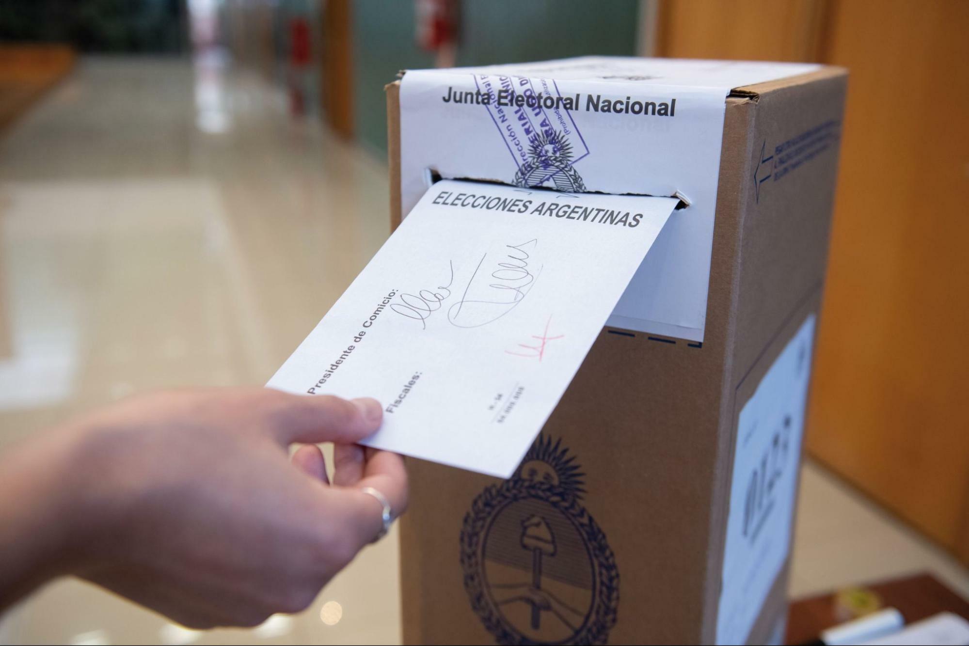 Mão deposita envelope com dizeres Elecciones Argentinas em urna feita de papelão