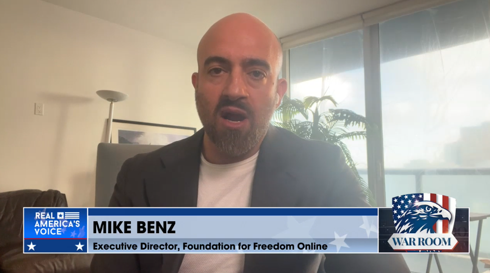Print mostra letreiro de podcast que informa, entre os logos do War Room e da Real America’s Voice, que Mike Benz é diretor executivo da Foundation for Freedom Online. Benz é um homem branco careca, com barba e sobrancelhas grossas, que veste paletó cinza sobre camiseta branca. Ao fundo se vê imagem que remete à sala de um apartamento.