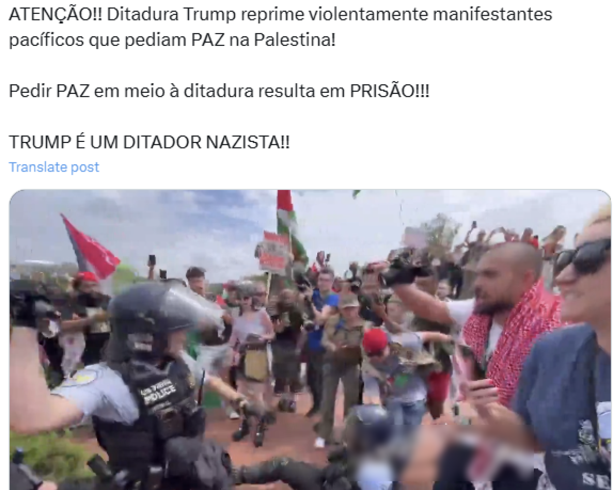 A imagem é um frame de um vídeo que mostra uma cena de confronto entre policiais e manifestantes. No primeiro plano, um policial com capacete e viseira está segurando um cassetete em uma posição de ação. Ao fundo, há um grupo de manifestantes segurando bandeiras da Palestina, em tons de verde, vermelho, preto e branco, e cartazes. Alguns estão levantando os braços, outros seguram câmeras. O ambiente está ao ar livre, com céu claro.