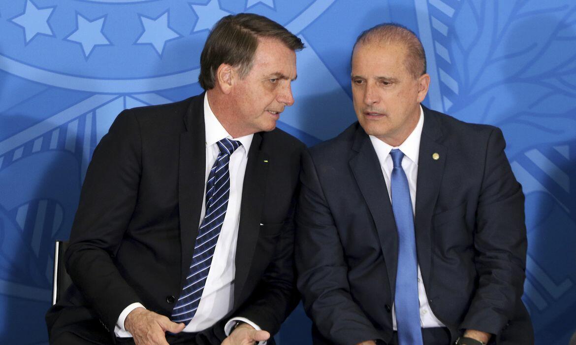 Foto mostra o ex-presidente Jair Bolsonaro (à esq.) — homem de pele branca e cabelo castanho que usa um terno preto, camisa branca e uma gravata listrada azul — ao lado de Onyx Lorenzoni (à dir.) — homem de pele branca e calvo, que usa um terno azul marinho, camisa branca e gravata azul