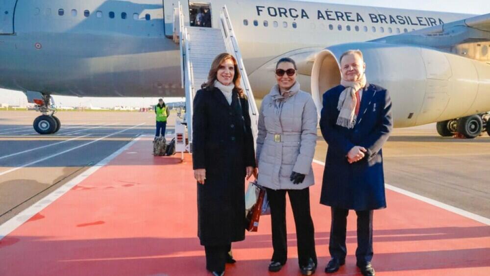 Foto mostra Janja, de óculos escuros e casaco cinza, ao lado de duas pessoas não públicas. Ao fundo, é possível ver um avião com a frase ‘Força Aérea Brasileira’.