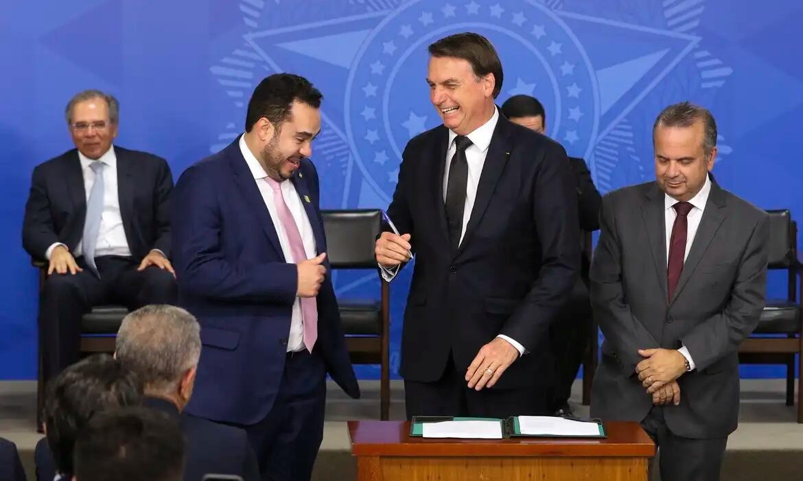 Foto mostra o momento que o então presidente Jair Bolsonaro — homem branco de cabelo castanho que aparece usando um terno e gravata preta — sanciona lei para combater fraudes no INSS durante cerimônia pública no Palácio do Planalto em 2019 