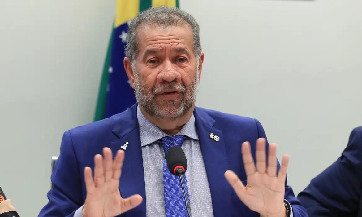 Foto mostra ex-ministro da Previdência Social, Carlos Lupi  — homem branco de cabelo e barba grisalhos usando um terno e gravata azul marinho e camisa social azul e branca quadriculada.