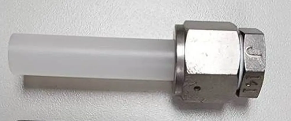 Imagem de uma peça de metal presa a um tubo branco. A peça metálica tem forma hexagonal, parecida com uma porca, e está fixando o tubo. O fundo é claro e liso.