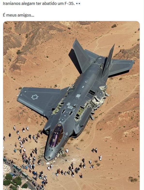 Imagem de um avião de caça F-35 cinza escuro acidentado, caído sobre uma área desértica. Partes da fuselagem estão danificadas e abertas, revelando o interior da aeronave. Ao redor do avião, diversas pessoas estão aglomeradas, observando os destroços.