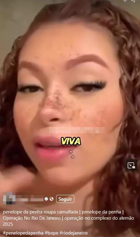 Uma captura de tela de um vídeo exibe o rosto de uma mulher em primeiro plano, identificada na legenda como 'penelope da penha'. Ela possui pele parda, cabelo castanho e cacheado, e pequenas sardas no nariz e bochechas. A mulher tem um piercing de metal com duas esferas pequenas abaixo do lábio inferior. A palavra 'VIVA' está sobreposta em letras maiúsculas amarelas na parte inferior do rosto. Abaixo da imagem, um texto de legenda inclui as frases 'penelope da penha roupa camuflada', 'Operação No Rio De Janeiro' e 'operação no complexo do alemão 2025', seguidas por hashtags.