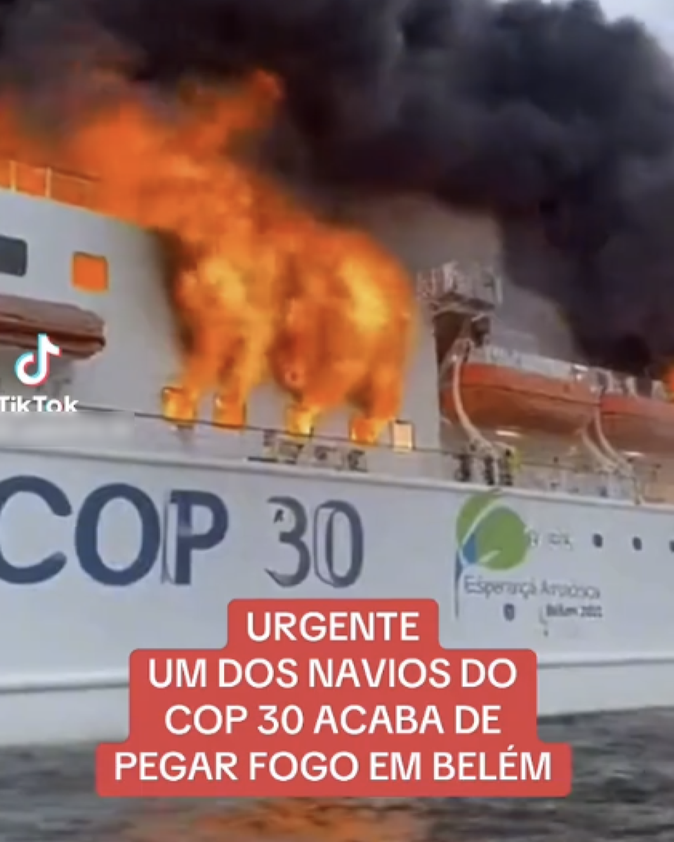 A imagem mostra um navio branco em chamas, com grandes labaredas alaranjadas e fumaça preta saindo da parte superior da embarcação. Na lateral do navio está escrito em letras grandes ‘COP 30’. Mais à frente, há um logotipo com o texto ‘Esperança Amazônica Belém 2025’. No canto inferior esquerdo aparece o ícone do TikTok. Sobre a imagem, há uma faixa vermelha com letras brancas que diz: ‘URGENTE UM DOS NAVIOS DO COP 30 ACABA DE PEGAR FOGO EM BELÉM’.