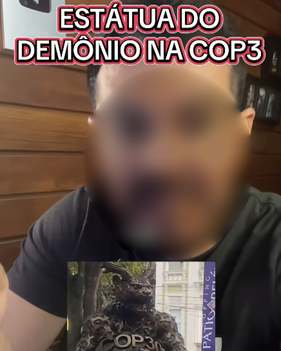 A imagem mostra uma pessoa em primeiro plano, com o rosto desfocado. Ela veste uma camiseta escura e está em um ambiente interno com paredes de madeira. Na parte superior da imagem, há um texto grande que diz: 'ESTÁTUA DO DEMÔNIO NA COP3'. No canto inferior da imagem, aparece um quadro menor exibindo a foto de uma escultura de aparência fantástica e detalhes ornamentados, posicionada ao ar livre, com árvores e parte de um prédio ao fundo.