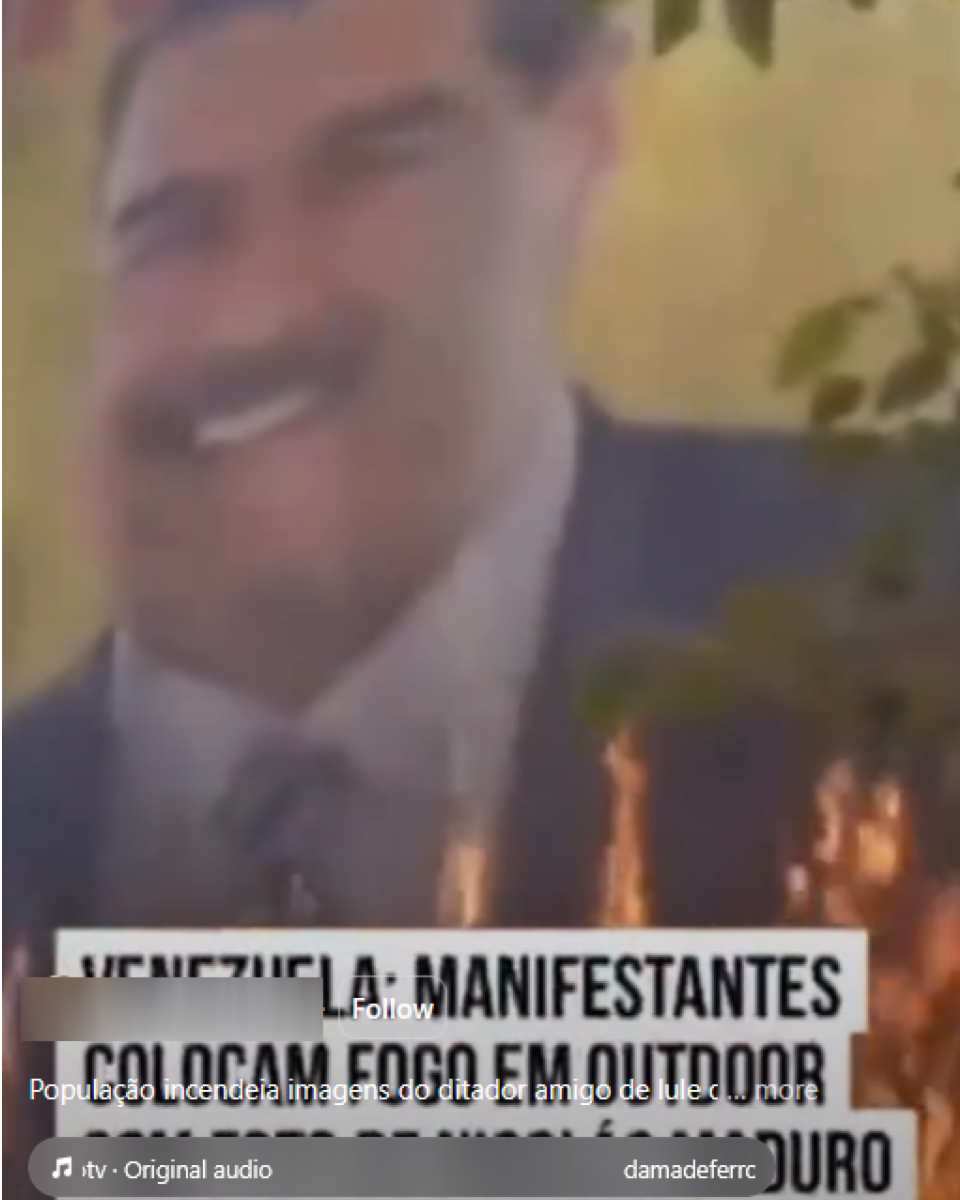 magem mostra um close desfocado de um outdoor em ambiente externo, exibindo o rosto de Nicolás Maduro — homem de pele morena, cabelo escuro e bigode, vestindo terno escuro, camisa clara e gravata, com expressão facial parcialmente visível devido à baixa nitidez. À frente do painel, há chamas em tons de laranja e amarelo subindo na parte inferior da imagem, sugerindo fogo próximo à estrutura, enquanto folhas de árvores aparecem nas laterais superiores. Sobre a cena, há elementos gráficos típicos de uma rede social, incluindo um texto parcialmente visível que menciona ‘VENEZUELA: MANIFESTANTES colocam fogo em outdoor’.