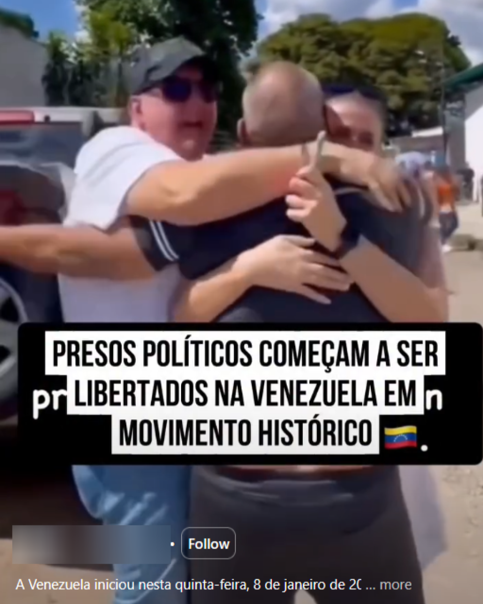 Imagem mostra uma cena ao ar livre durante o dia em que três homens adultos se abraçam no centro do enquadramento. Um deles, de pele clara, usa boné escuro, óculos de sol e camiseta branca; outro, de pele clara e cabelo raspado, veste camiseta escura; o terceiro, também de pele clara, aparece parcialmente atrás, usando camiseta escura e óculos. Eles estão próximos a veículos estacionados, com árvores e construções ao fundo. Sobre a imagem, há uma faixa preta com texto em letras brancas que diz ‘Presos políticos começam a ser libertados na Venezuela em movimento histórico.’