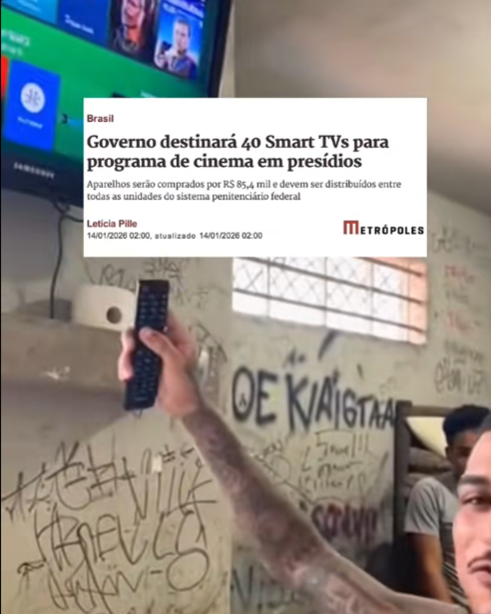 Frame de vídeo mostra, em primeiro plano, um homem jovem de pele morena, com cabelo curto escuro e bigode, sem camisa, exibindo tatuagens no braço, levantando um controle remoto em direção a uma televisão fixada na parte superior esquerda. No fundo, há pelo menos dois homens sentados, também de pele morena, usando camisetas casuais, em um espaço que lembra uma cela ou quarto coletivo. Sobre a imagem, há um recorte de matéria do site Metrópoles com o título ‘Governo destinará 40 Smart TVs para programa de cinema em presídios’