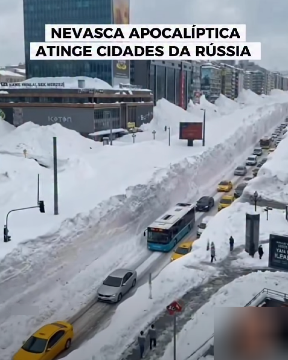 Vista aérea de avenida urbana coberta por neve, com montes altos de neve acumulada nas laterais, formando corredores ao longo da via. A rua está parcialmente liberada para o tráfego, com carros e um ônibus circulando em fila, enquanto pedestres aparecem em calçadas estreitas próximas aos bancos de neve; ao fundo, há prédios comerciais e residenciais. No topo da imagem, há um texto em caixa alta que diz ‘NEVASCA APOCALÍPTICA ATINGE CIDADES DA RÚSSIA’ e, na parte inferior, uma legenda em branco sobre faixa escura afirma ‘Sinais dos tempos! 2026 começou de forma extraordinária!’