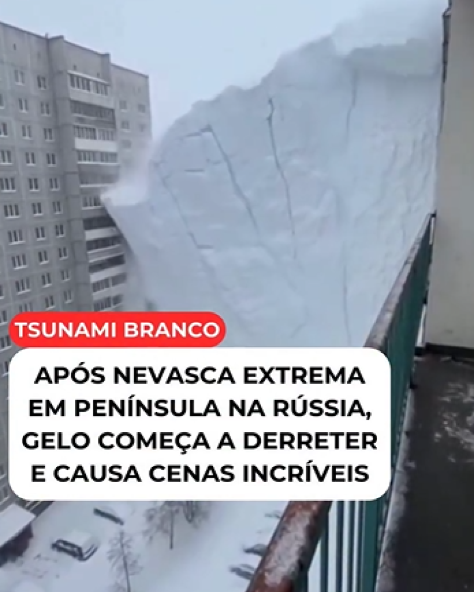 Cena vista de uma varanda de prédio em área residencial coberta de neve, com corrimão metálico verde em primeiro plano e edifícios altos cinzentos ao fundo. À direita, uma grande placa de gelo aparece inclinada para fora da estrutura do prédio, ocupando parte do enquadramento, enquanto abaixo se veem ruas e áreas entre edifícios recobertas por neve. Sobre a imagem, há um selo vermelho com o texto ‘TSUNAMI BRANCO’ e, em uma caixa branca, a frase ‘APÓS NEVASCA EXTREMA EM PENÍNSULA NA RÚSSIA, GELO COMEÇA A DERRETER E CAUSA CENAS INCRÍVEIS.’