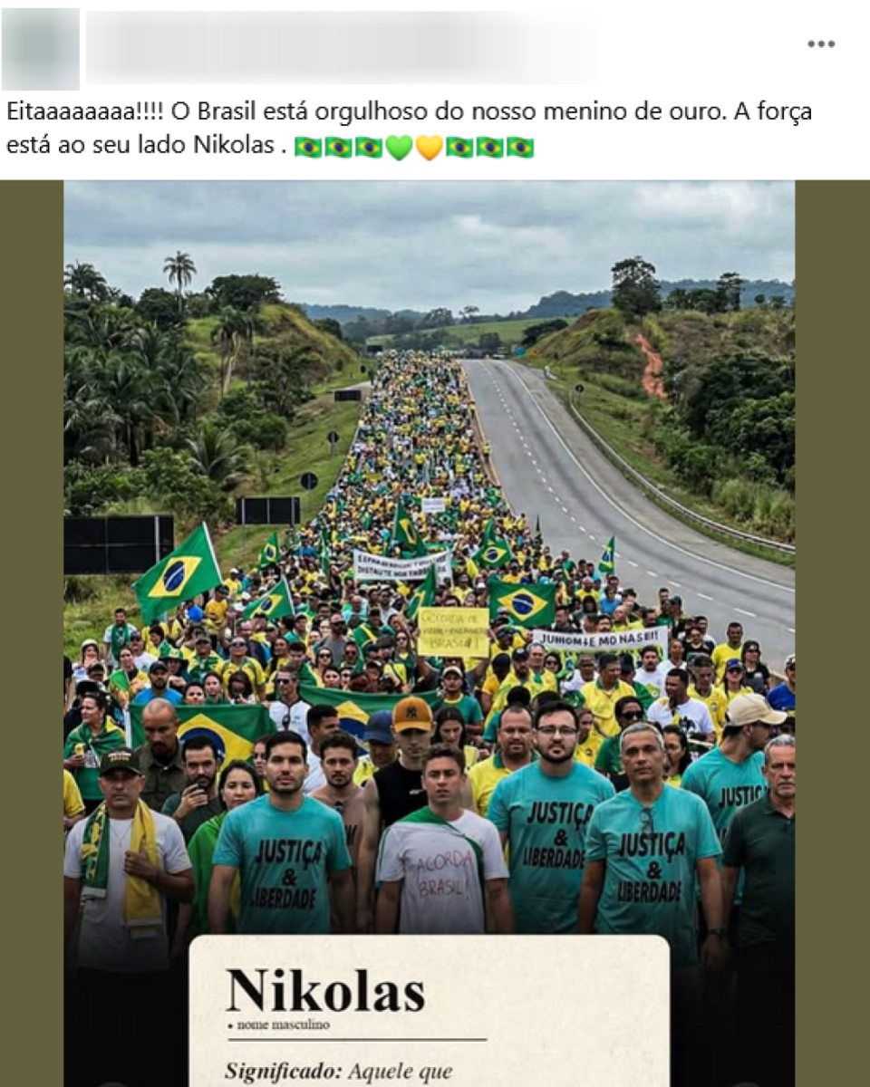 Manifestação em rodovia, com grande multidão ao fundo vestida majoritariamente de verde e amarelo e carregando bandeiras do Brasil. Há também faixas e cartazes; no alto, aparece um cartaz com ‘#BOLSONARO’, e outros com palavras como ‘liberdade’ e ‘Justiça’ (parcialmente visíveis). Em primeiro plano, Nikolas Ferreira caminha no centro, usando camiseta branca e calça jeans, com expressão séria. À direita dele, outro homem aparece em destaque com roupa preta, boné e óculos pendurados na gola da camisa. Atrás, várias pessoas seguram bandeiras do Brasil.