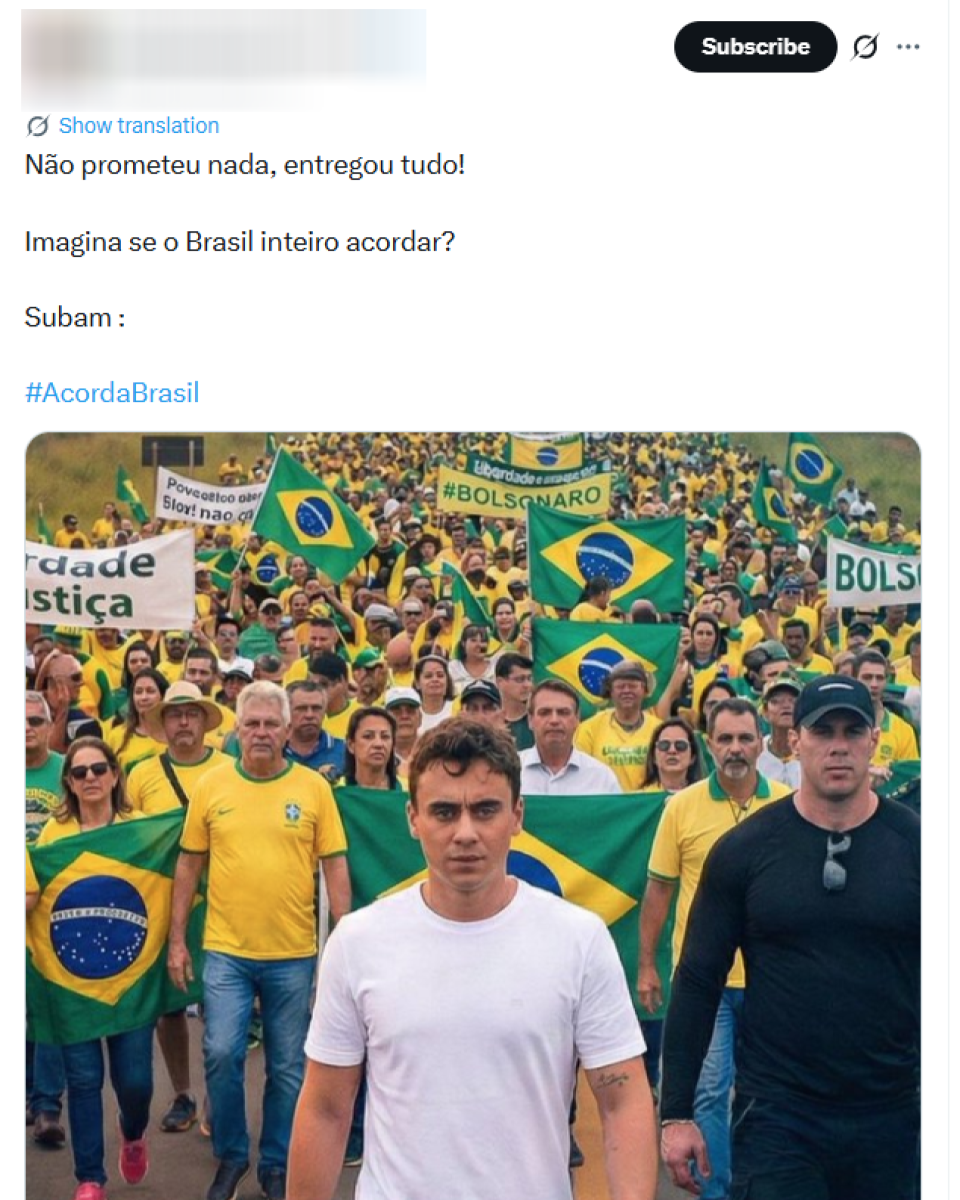Manifestação em rodovia, com grande multidão ao fundo vestida majoritariamente de verde e amarelo e carregando bandeiras do Brasil. Há também faixas e cartazes; no alto, aparece um cartaz com ‘#BOLSONARO’, e outros com palavras como ‘liberdade’ e ‘Justiça’ (parcialmente visíveis). Em primeiro plano, Nikolas Ferreira caminha no centro, usando camiseta branca e calça jeans, com expressão séria. À direita dele, outro homem aparece em destaque com roupa preta, boné e óculos pendurados na gola da camisa. Atrás, várias pessoas seguram bandeiras do Brasil.