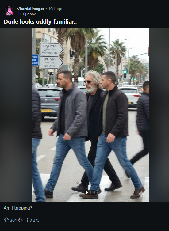 Publicação no Reddit. Post compartilha imagem de homem idoso, de pele clara, cabelo grisalho médio e barba grisalha, usando óculos escuros, camiseta escura e jaqueta escura, caminhando em uma rua acompanhado por outros homens de pele clara. Ao fundo, há carros, placas de trânsito com escrita supostamente em hebraico, postes, árvores e prédios. Legenda: Foto gerada por IA foi originalmente compartilhada no Reddit em comunidade dedicada a conteúdos sintéticos (Reprodução/Reddit)