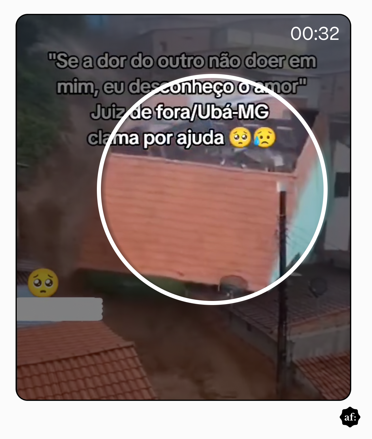 Área urbana em encosta com casas de alvenaria próximas umas das outras, com telhados de cerâmica laranja, enquanto uma enxurrada de lama marrom desce com força por uma rua estreita ao lado das construções. Uma casa verde aparece em destaque no centro, com a água barrenta passando junto às paredes, enquanto postes e fiação elétrica estão visíveis no primeiro plano.