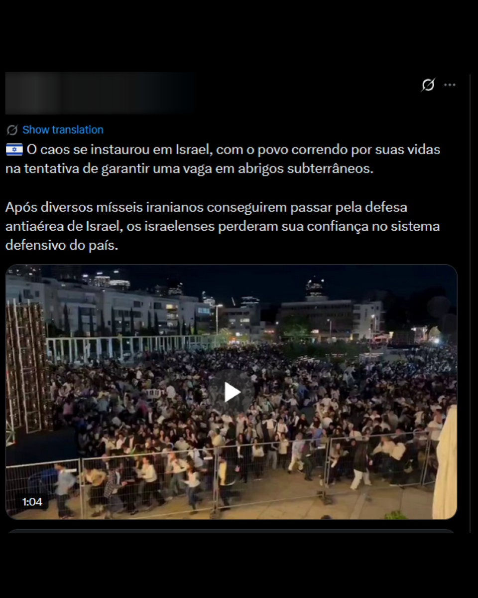 Post do X mostra multidão reunida em espaço urbano durante a noite, cercada por grades metálicas e prédios iluminados ao fundo. As pessoas aparecem caminhando rapidamente ou olhando em direção à frente, enquanto outras estão paradas próximas a barreiras. No topo da publicação, há um texto que menciona caos em Israel e a busca por abrigo subterrâneo após ataques com mísseis.