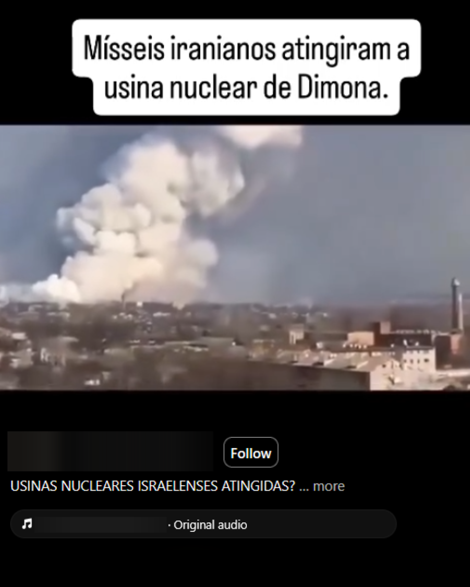 Paisagem urbana vista à distância, com casas e edifícios baixos espalhados por área plana. Ao fundo, uma grande coluna de fumaça branca e cinza se eleva do solo, formando uma nuvem que ocupa boa parte do céu. Na parte superior da publicação, há um texto que afirma: ‘Mísseis iranianos atingiram a usina nuclear de Dimona’.