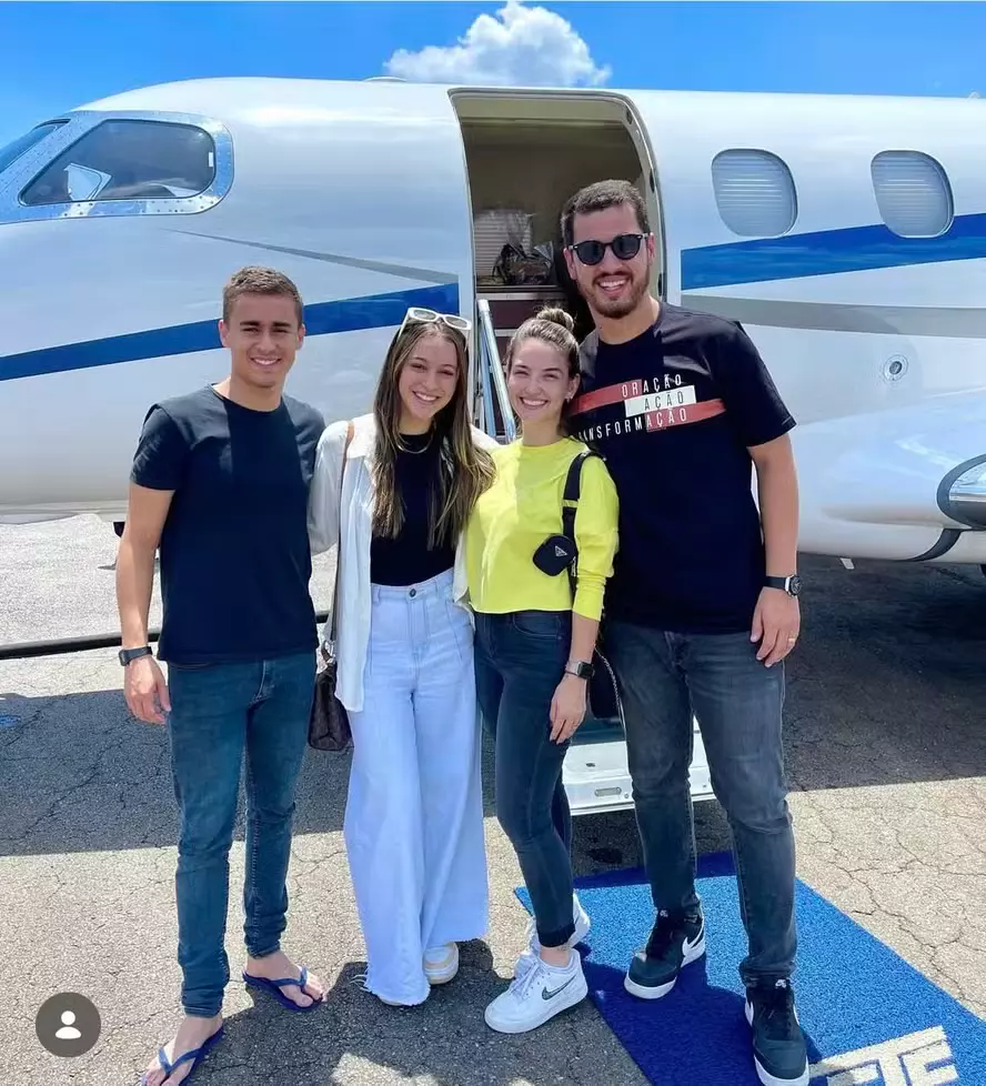Foto mostra quatro pessoas em pé e sorrindo em frente a um jato executivo. À esquerda está o deputado Nikolas Ferreira — homem de pele clara e cabelos curtos e castanhos, vestindo camiseta preta, calça jeans e chinelos azuis. Ao seu lado, está a influenciadora Jey Reis, mulher com cabelos castanhos longos e óculos de sol na cabeça, usando camisa preta com uma blusa branca aberta por cima e calça jeans larga. A terceira pessoa é Mariel Batista, mulher com cabelo preso em coque, vestindo blusa amarela de mangas compridas, calça jeans escuras e tênis brancos. À direita, está o pastor Guilherme Batista, homem de pele clara com barba curta e cabelos pretos, óculos de sol escuros e vestindo uma camiseta preta com estampa branca e vermelha, calça jeans cinzas e tênis pretos.