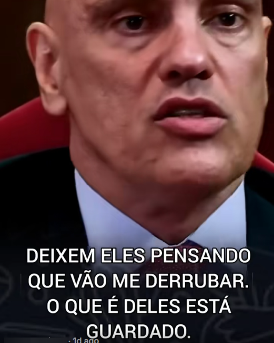 Ministro do STF Alexandre de Moraes — homem de pele clara, calvo e sem barba — em close, com expressão séria e olhando à frente. Ele veste terno escuro, camisa clara e gravata e está sentado em uma cadeira de encosto vermelho em ambiente que lembra uma sessão oficial. Sobre a imagem, há um texto que diz: ‘DEIXEM ELES PENSANDO QUE VÃO ME DERRUBAR. O QUE É DELES ESTÁ GUARDADO.’