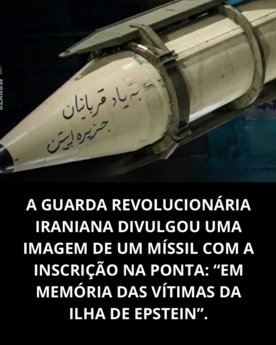 A imagem mostra a parte frontal de um míssil de cor clara, preso a uma estrutura metálica de suporte, com inscrições em caracteres árabes pintadas na superfície. O objeto aparece em posição inclinada contra um fundo escuro. Na metade inferior da imagem há um texto em letras brancas que diz: ‘A GUARDA REVOLUCIONÁRIA IRANIANA DIVULGOU UMA IMAGEM DE UM MÍSSIL COM A INSCRIÇÃO NA PONTA: EM MEMÓRIA DAS VÍTIMAS DA ILHA DE EPSTEIN.’.