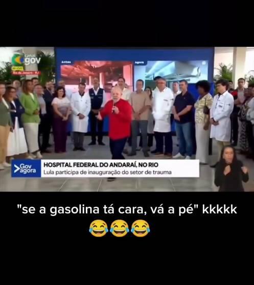 A imagem mostra um quadro de uma transmissão televisiva do programa ‘Gov Agora’. No centro aparece o presidente Luiz Inácio Lula da Silva — homem idoso de pele clara, cabelo curto branco e barba branca — vestindo um casaco vermelho e segurando um microfone enquanto fala. Ele está em pé em um espaço interno de hospital, cercado por várias pessoas ao fundo, incluindo profissionais de saúde usando jalecos brancos e outras pessoas com roupas casuais. Um texto na tela diz: ‘Hospital Federal do Andaraí, no Rio — Lula participa de inauguração do setor de trauma’. No canto inferior direito há uma intérprete de Libras — mulher de pele clara, cabelo escuro e roupa preta. Abaixo do quadro da transmissão aparece a frase: ‘se a gasolina tá cara, vá a pé’ kkkkk’, acompanhada de três emojis de rosto chorando de rir.