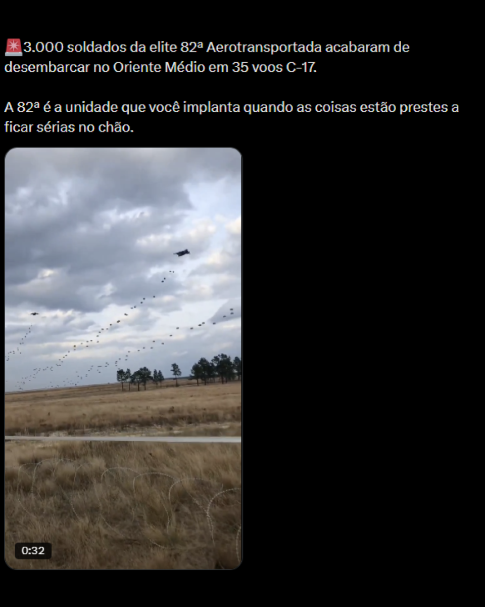 A imagem mostra uma publicação em fundo preto com texto em português na parte superior. O texto diz: ‘3.000 soldados da elite 82ª Aerotransportada acabaram de desembarcar no Oriente Médio em 35 voos C-17. A 82ª é a unidade que você implanta quando as coisas estão prestes a ficar sérias no chão’. Abaixo do texto há um vídeo em formato vertical. No quadro do vídeo, aparece um céu nublado com nuvens cinzentas e vários pontos escuros alinhados no ar formando linhas diagonais, descendo em direção ao solo. Há também uma aeronave visível no céu. Na parte inferior do vídeo, aparece uma paisagem com vegetação seca, de cor amarelada, e algumas árvores ao fundo. No canto inferior esquerdo do vídeo, há um marcador de tempo indicando 0:32.
