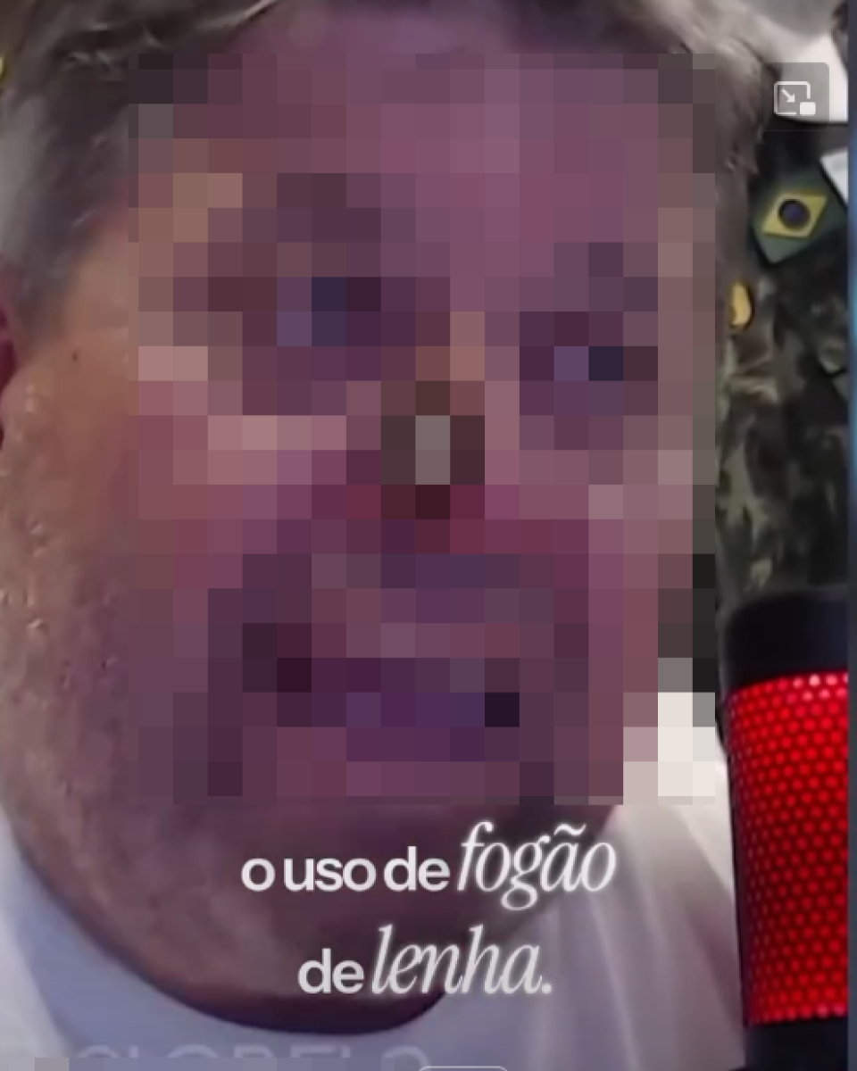 Close de homem com o rosto pixelado, dificultando a identificação de suas características faciais; é possível notar pele clara e cabelo curto em tom claro. Ele está próximo a um microfone cilíndrico com iluminação vermelha, sugerindo gravação de áudio ou vídeo. Ao fundo, há elementos desfocados de um ambiente interno. Sobre a imagem, aparece o texto: ‘o uso de fogão de lenha.’ e, na parte inferior, um trecho de legenda que diz: ‘Nova Lei Criminaliza Uso de Fogão de Lenha no Brasil’.