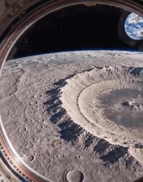 A imagem mostra a superfície da Lua vista através de uma janela circular, com diversas crateras visíveis, incluindo uma cratera grande e profunda em primeiro plano. Ao fundo, aparece o espaço escuro com estrelas e o planeta Terra parcialmente iluminado. A borda da janela indica o ambiente interno de uma nave espacial.