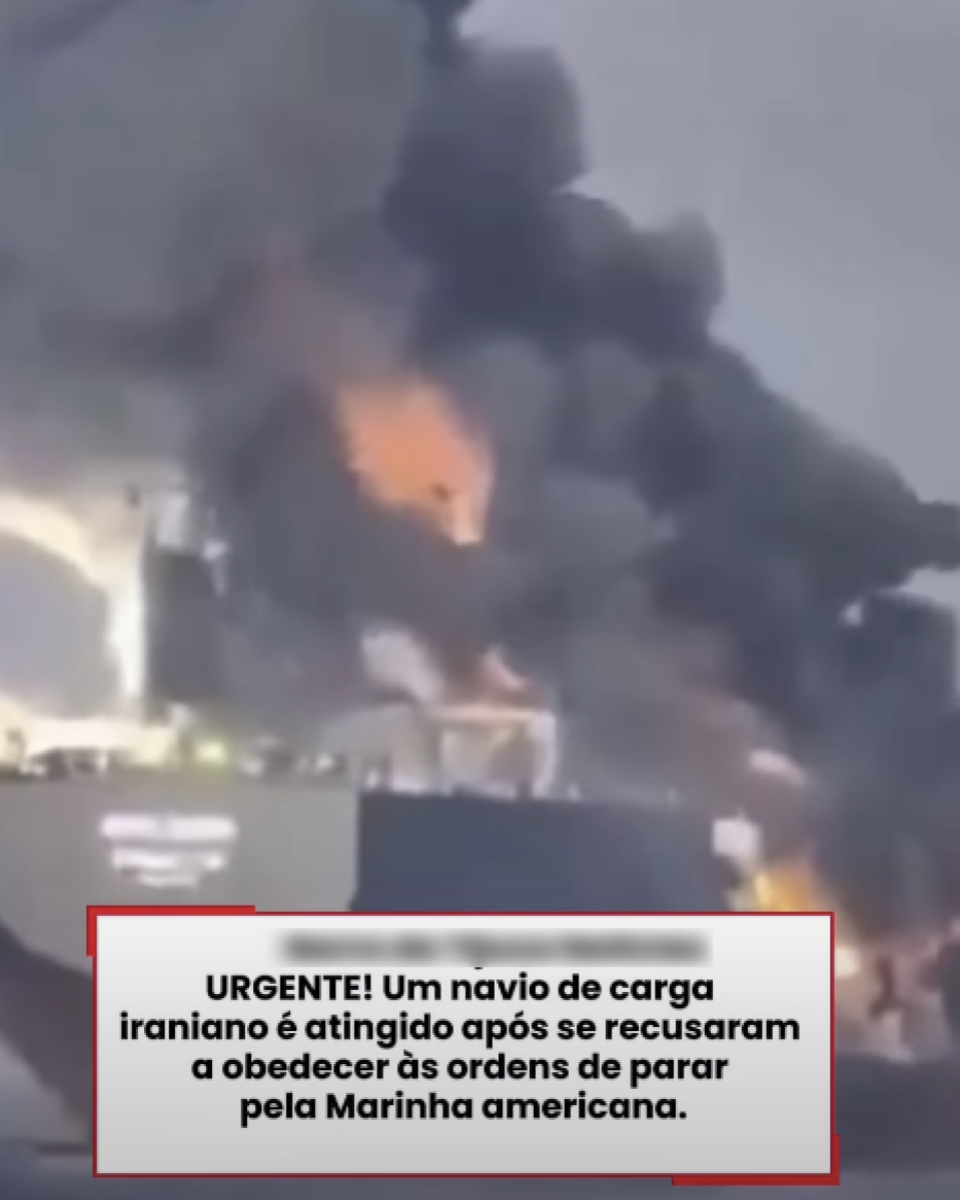 Cena com uma grande coluna de fumaça escura subindo para o céu, com chamas alaranjadas visíveis na base, similar a um incêndio em uma embarcação. O ambiente ao redor é pouco nítido, com tons acinzentados e baixa definição. Na parte inferior da imagem há um texto que diz: ‘URGENTE! Um navio de carga iraniano é atingido após se recusarem a obedecer às ordens de parar pela Marinha americana’.