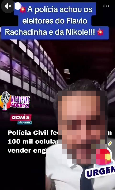Imagem mostra homem com rosto pixelado — ele aparenta ter pele clara, cabelo curto escuro e barba — usando camisa branca e gravata escura, em primeiro plano. Ao fundo, há um cenário que lembra um corredor com várias telas ou painéis iluminados nas paredes. No topo da imagem, há um texto em destaque que diz: ‘A polícia achou os eleitores do Flavio Rachadinha e da Nikole!!!’. No canto inferior esquerdo, aparece um logotipo com um microfone e a expressão ‘Microfone Aberto’, além de um selo com ‘Goiás’. Na parte inferior, há um texto parcialmente visível que menciona ‘Polícia Civil’ e ‘100 mil celulares’, acompanhado de um selo gráfico com a palavra ‘URGENTE’.