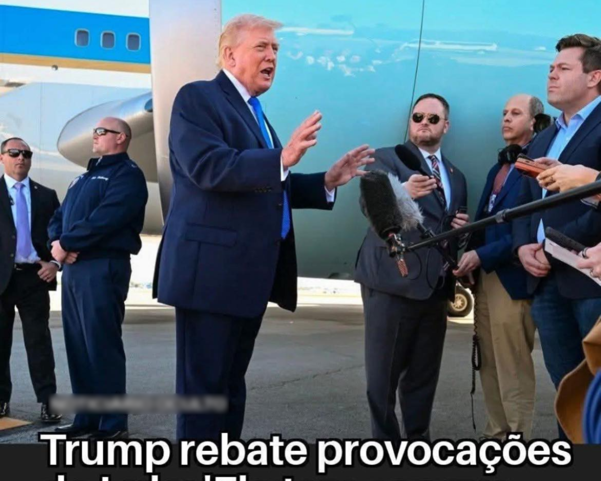 Imagem mostra grupo de homens ao lado de avião em área externa. No centro, aparece Donald Trump, um homem branco vestindo terno escuro e gravata azul, com mãos levantadas em frente ao corpo. À direita, há outros homens também de terno, um deles usando óculos escuros e segurando um microfone direcionado ao homem central, enquanto outro segura um gravador. À esquerda, dois homens de terno e óculos escuros estão posicionados próximos à aeronave. Na parte inferior da imagem, há uma faixa escura com texto em letras brancas que diz ‘Trump rebate provocações de Lula: 'Ele tem sangue de lampião a álcool'’.