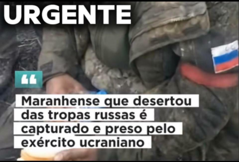 Vídeo gerado por IA mostra homem com feições abatidas, vestindo uniforme militar verde-oliva sujo. No braço da jaqueta há um emblema com a bandeira da Rússia e uma braçadeira vermelha. Ele está sentado ao ar livre, segurando o que parece ser um pedaço de pão. Ao fundo, à esquerda, vê-se parcialmente as pernas de outra pessoa em uniforme e parte de um fuzil. A imagem possui várias sobreposições de texto. Na parte inferior, dentro de blocos brancos, está escrito: ‘	‘Maranhense que desertou das tropas russas é capturado e preso pelo exército ucraniano’.