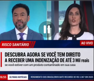 Captura de tela de telejornal com dois apresentadores divididos em telas lado a lado. À esquerda, um homem de terno azul e gravata aparece olhando para baixo; à direita, uma mulher de cabelo escuro fala diante da câmera. Na parte inferior, uma faixa vermelha e azul com o título ‘RISCO SANITÁRIO’ acompanha um texto em destaque: ‘DESCUBRA AGORA SE VOCÊ TEM DIREITO A RECEBER UMA INDENIZAÇÃO DE ATÉ 3 Mil reais’, seguido da frase ‘se você estiver com um produto contaminado em sua casa’. No canto superior direito aparece a indicação ‘AO VIVO’.