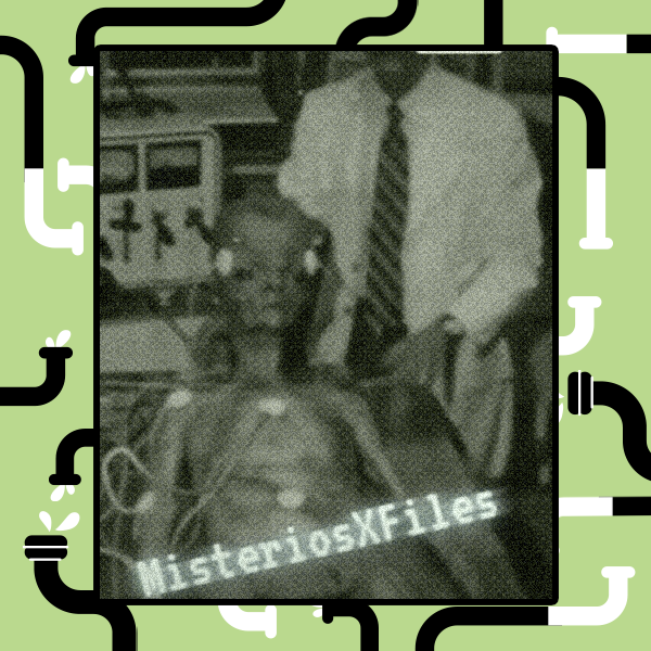 Imagem em preto e branco com forte granulação, simulando uma filmagem antiga ou de baixa qualidade. No centro, uma criatura humanoide magra, de aparência alienígena, está deitada em uma maca cercada por equipamentos médicos e fios conectados ao corpo. Ao fundo, um homem de camisa clara e gravata aparece parcialmente visível atrás da maca. No canto inferior da imagem, há a inscrição ‘MisteriosXFiles’. 