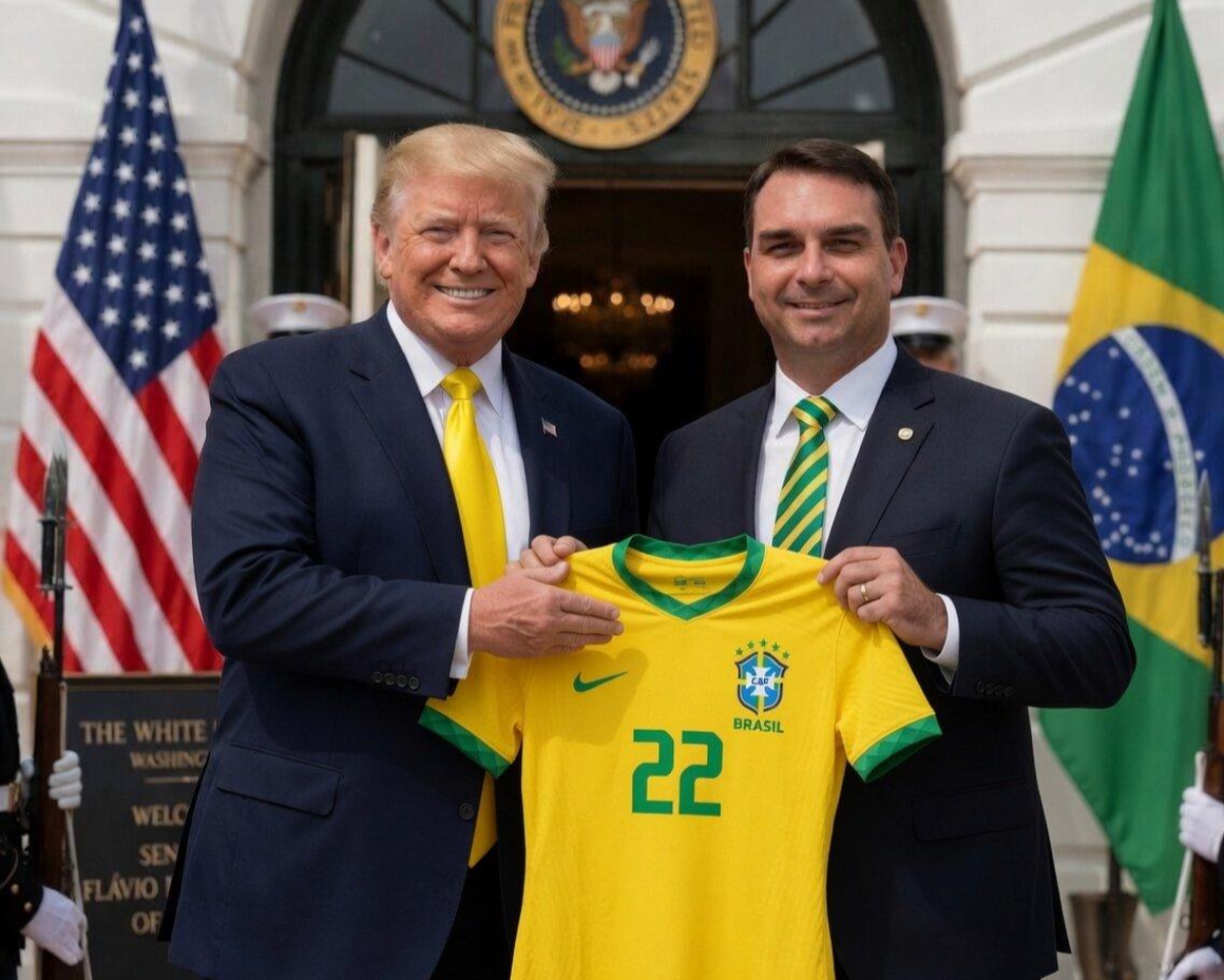 Imagem gerada artificialmente mostra dois homens, Donald Trump e Flávio Bolsonaro, em pé lado a lado em frente à entrada de um prédio com colunas brancas e o selo presidencial dos Estados Unidos acima da porta. À esquerda, Trump usa terno azul-marinho, camisa branca e gravata amarela, e está sorrindo para a câmera. À direita, Flávio Bolsonaro usa terno escuro, camisa branca e gravata listrada em verde e amarelo, e também aparece sorrindo. Os dois seguram juntos uma camisa amarela da seleção brasileira com detalhes verdes e o número ‘22’ estampado na frente. Ao fundo, aparecem as bandeiras dos Estados Unidos e do Brasil posicionadas em lados opostos da entrada, além de dois guardas parcialmente visíveis nas laterais.