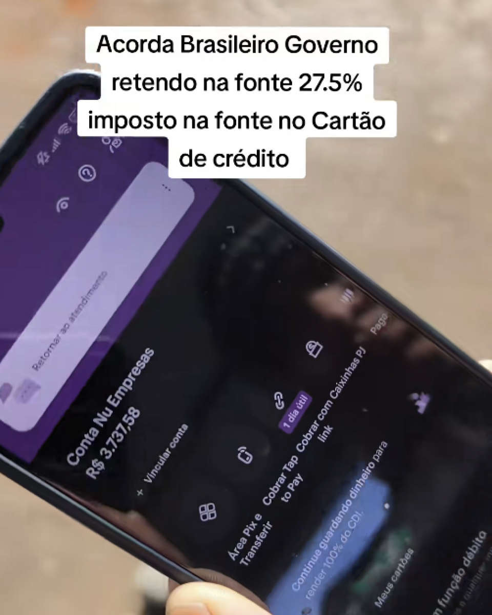 A imagem mostra um celular sendo segurado por uma mão, inclinado na diagonal. Na tela está aberto o aplicativo do Nubank Empresas com interface em tons de roxo e fundo escuro. Na parte superior da imagem há um bloco de texto em fundo branco com letras pretas distribuídas em várias linhas, dizendo: ‘Acorda Brasileiro Governo retendo na fonte 27.5% imposto na fonte no Cartão de crédito’. Na tela do celular aparece o nome da conta ‘Conta Nu Empresas’ e o saldo de ‘R$ 3.737,58’. Abaixo há opções como ‘Área Pix e Transferir’, ‘Cobrar Tap to Pay”, ‘Cobrar com link’, ‘Caixinhas PJ’ e outras funções do aplicativo. Também é possível ver uma barra de busca com o texto ‘Retornar ao atendimento’ e diversos ícones na parte superior da interface. O fundo ao redor do celular está desfocado em tons claros de bege e marrom.