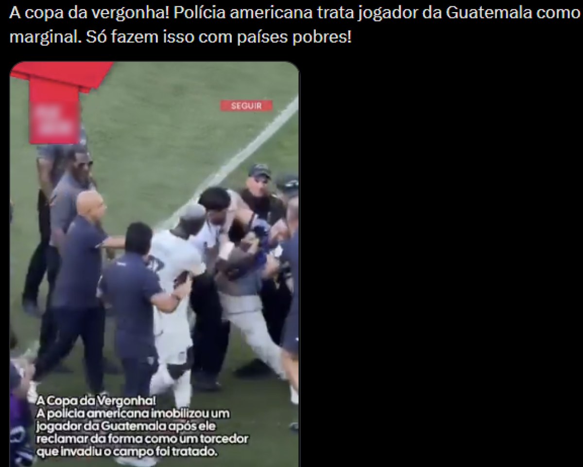 Captura de tela com fundo preto. Na parte superior há um texto em letras brancas que diz: 'A copa da vergonha! Polícia americana trata jogador da Guatemala como marginal. Só fazem isso com países pobres!'. Abaixo do texto aparece um vídeo em formato vertical. A gravação mostra um grupo de pessoas em um gramado verde. Entre elas há indivíduos usando roupas escuras e bonés. Alguns estão segurando os braços e o corpo de um homem enquanto outros se aproximam ao redor. Ao fundo é possível ver uma linha branca marcada no gramado.