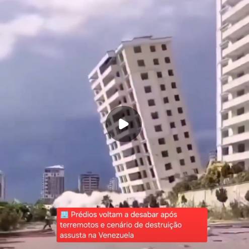 Uma captura de tela de vídeo mostra um edifício alto de cor clara, com múltiplas janelas e varandas, inclinado acentuadamente para a esquerda sob um céu nublado. Na base da estrutura, ergue-se uma grande e densa nuvem de poeira clara. No canto inferior esquerdo, há uma figura humana distante vestindo blusa clara e calça escura, porém, devido à baixa resolução e à distância, não é possível identificar características físicas detalhadas. No centro da imagem encontra-se um ícone circular escuro com um símbolo de reprodução de vídeo em branco. Na parte inferior, sobreposta à cena, há uma tarja vermelha com o texto em letras brancas, precedido por um emoji de edifício: 'Prédios voltam a desabar após terremotos e cenário de destruição assusta na Venezuela'. 