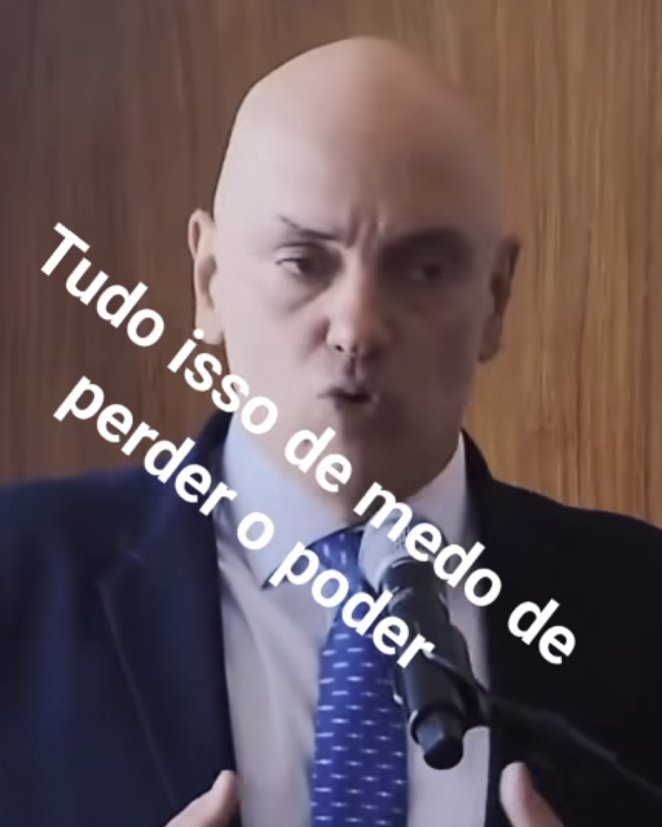 A imagem mostra Alexandre de Moraes, um homem careca, vestindo terno escuro, camisa branca e gravata azul com pequenos pontos brancos, falando diante de um microfone sobre um púlpito. Ao fundo há um painel de madeira em tom marrom. Ele aparece com expressão séria e está gesticulando com as mãos enquanto fala. Sobre a imagem foi adicionada, na diagonal e em letras brancas grandes, a frase: 'Tudo isso de medo de perder o poder', cobrindo boa parte do rosto, do tórax e do microfone. 