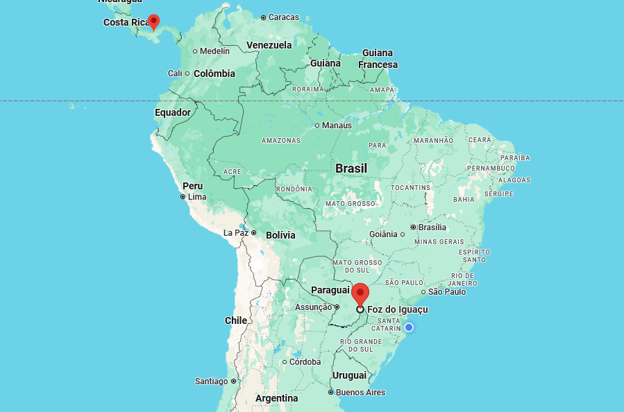 Mapa cartográfico digital abrangendo a América do Sul e parte da América Central, com territórios continentais coloridos em tons de verde e bege e áreas oceânicas em azul-claro. As divisas políticas entre os países e os limites estaduais no Brasil são representados por linhas finas. O mapa contém diversos textos de identificação geográfica, destacando-se a presença de dois ícones vermelhos de localização em formato de pino: um situado no Panamá, região da América Central, e outro no sul do território brasileiro, ao lado da inscrição 'Foz do Iguaçu'