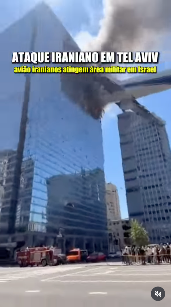 Captura de tela de um vídeo na qual um grande avião comercial aparece colidindo com a fachada de vidro de um arranha-céu moderno em uma área urbana. Muita fumaça escura sai do ponto de impacto no edifício. Na parte superior da imagem, há dois textos sobrepostos em letras garrafais: em branco, lê-se 'ATAQUE IRANIANO EM TEL AVIV' e, logo abaixo, em amarelo, 'avião iranianos atingem área militar em Israel'. Na parte inferior da rua, vêem-se veículos de emergência, como um caminhão de bombeiros, e algumas pessoas observando. No canto inferior direito, há um ícone de alto-falante mutado.