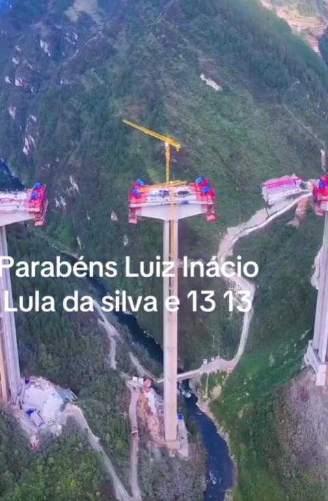 Fotografia aérea mostra a construção de um viaduto gigante com pilares extremamente altos sobre um vale montanhoso e um rio ao fundo. No centro da imagem, há um pilar com um guindaste amarelo no topo, e sobreposta ao centro da imagem consta a frase: