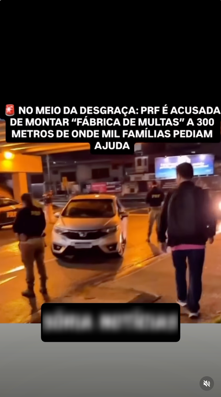 Captura de tela de um vídeo gravado à noite em uma rua iluminada. No centro, há um carro sedan de cor clara estacionado perto de policiais rodoviários federais. À esquerda, uma pessoa vestindo uniforme bege e jaqueta preta com a sigla 'PRF' nas costas observa a cena. À direita, um homem de costas caminha na calçada vestindo jaqueta preta, camiseta rosa e calça jeans. Na parte superior da imagem, há um texto em caixa alta e fundo preto que diz: '🚨 NO MEIO DA DESGRAÇA: PRF É ACUSADA DE MONTAR ‘FÁBRICA DE MULTAS’ A 300 METROS DE ONDE MIL FAMÍLIAS PEDIAM AJUDA'. Na parte inferior, há um retângulo preto cobrindo uma marca d'água borrada. No canto inferior direito, aparece o ícone de áudio mutado do Instagram.