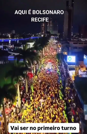 Imagem aérea, à noite, de uma grande multidão ocupando uma avenida à beira de um canal ou lago, com prédios altos e iluminados ao fundo. As pessoas parecem concentradas em torno de trios elétricos e há várias árvores, incluindo palmeiras, ao longo da via. Na parte superior, o texto diz AQUI É BOLSONARO RECIFE. Na parte inferior, uma caixa branca traz a frase Vai ser no primeiro turno.