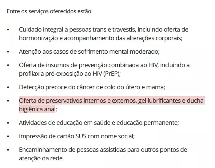 Uma captura de tela exibe um texto em letras pretas sobre um fundo branco, iniciado pela frase 'Entre os serviços oferecidos estão:', seguida por uma lista de oito itens organizados em marcadores. A lista elenca procedimentos e atendimentos de saúde, como cuidado integral a pessoas trans, prevenção ao HIV, detecção de câncer, saúde mental, impressão de cartão SUS com nome social, entre outros. O quinto tópico da lista contém o texto 'Oferta de preservativos internos e externos, gel lubrificantes e ducha higiênica anal;' e encontra-se inteiramente destacado com um realce de fundo na cor rosa claro.