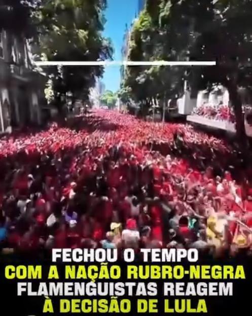 Uma imagem vertical exibe uma ampla via urbana arborizada ocupada por uma densa multidão durante o dia. A esmagadora maioria das pessoas veste roupas na cor vermelha, formando uma mancha contínua que se estende ao longo da avenida; devido à resolução e à distância, não é possível identificar características físicas individuais. Na metade superior da cena, uma fina linha horizontal branca sobrepõe a imagem. Na base, sobre um fundo escuro, o seguinte texto em letras maiúsculas está dividido em quatro linhas alternadas em branco e amarelo: 'FECHOU O TEMPO COM A NAÇÃO RUBRO-NEGRA FLAMENGUISTAS REAGEM À DECISÃO DE LULA'.  